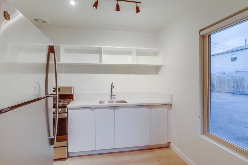 Vacant kitchen showing stainless gas range, quartz counters and open walnut-lit shelving
