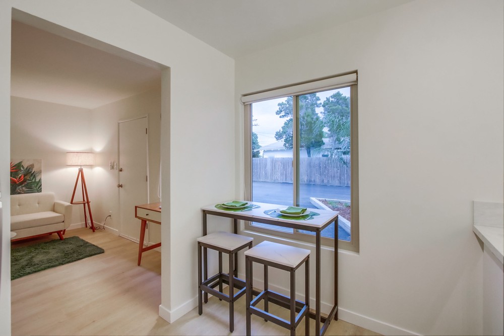 Breakfast bar with stools beside a sunny window, opening to a staged living room