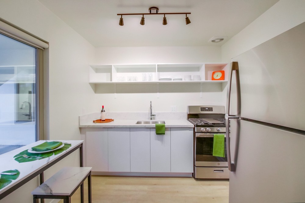 Staged kitchen with stainless gas range, refrigerator, quartz counters and walnut track lighting